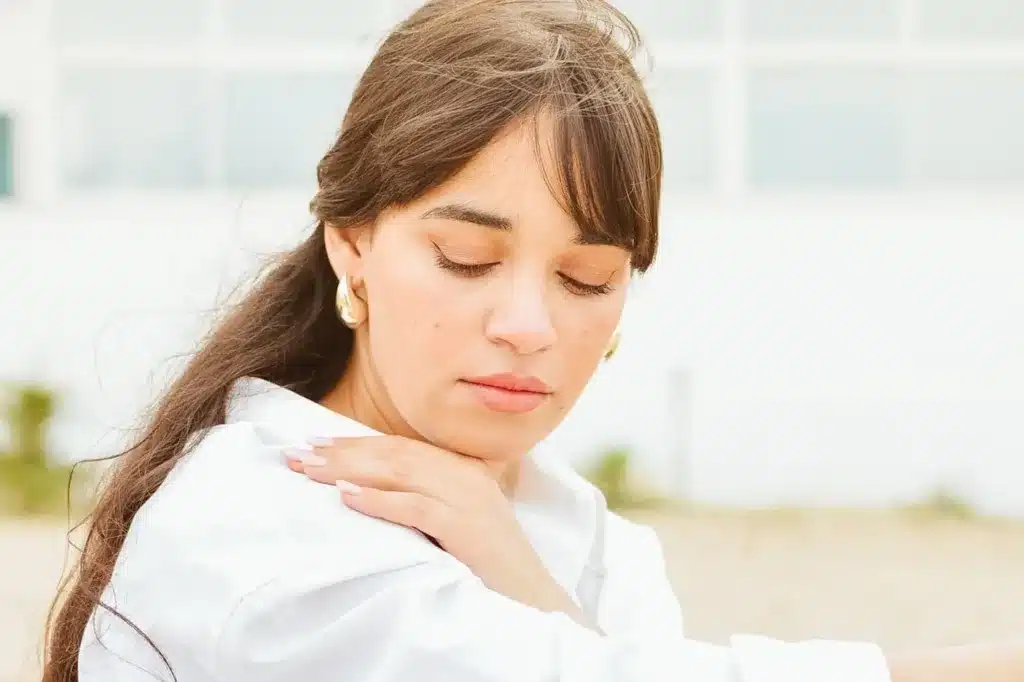 Personne portant la main à son épaule et sa nuque, près d’une fenêtre