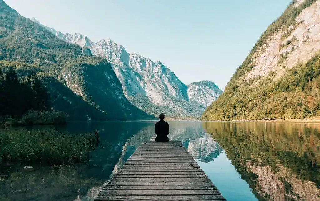 Personne assise au bout d’un ponton, face à un lac de montagne